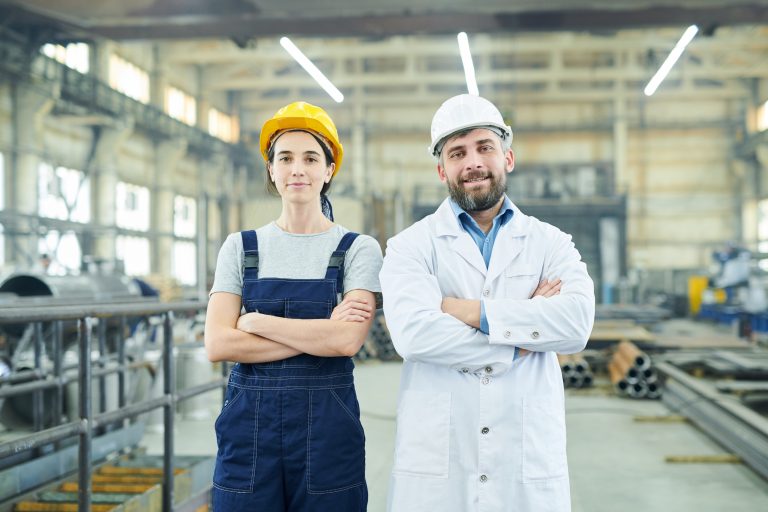 Waist up portrait of two modern factory workers looking at camera while posing in industrial workshop